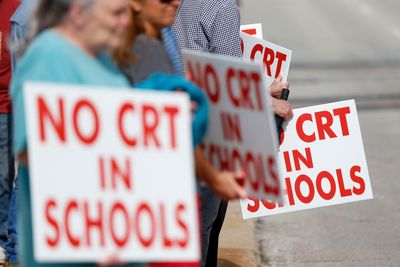 Image of protesters holding white signs that say no CRT in schools in red.